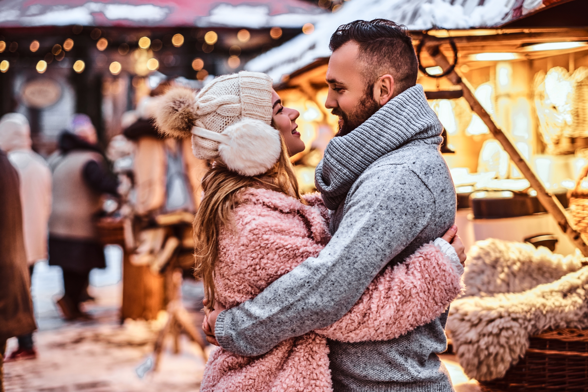 Attractive couple wearing warm clothes near a shop of a winter fair at a Christmas time Attractive couple wearing warm clothes near a shop of a winter fair at a Christmas time
